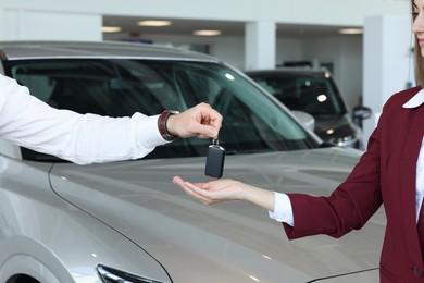 Photo of Salesman giving key to client near new car in salon, closeup