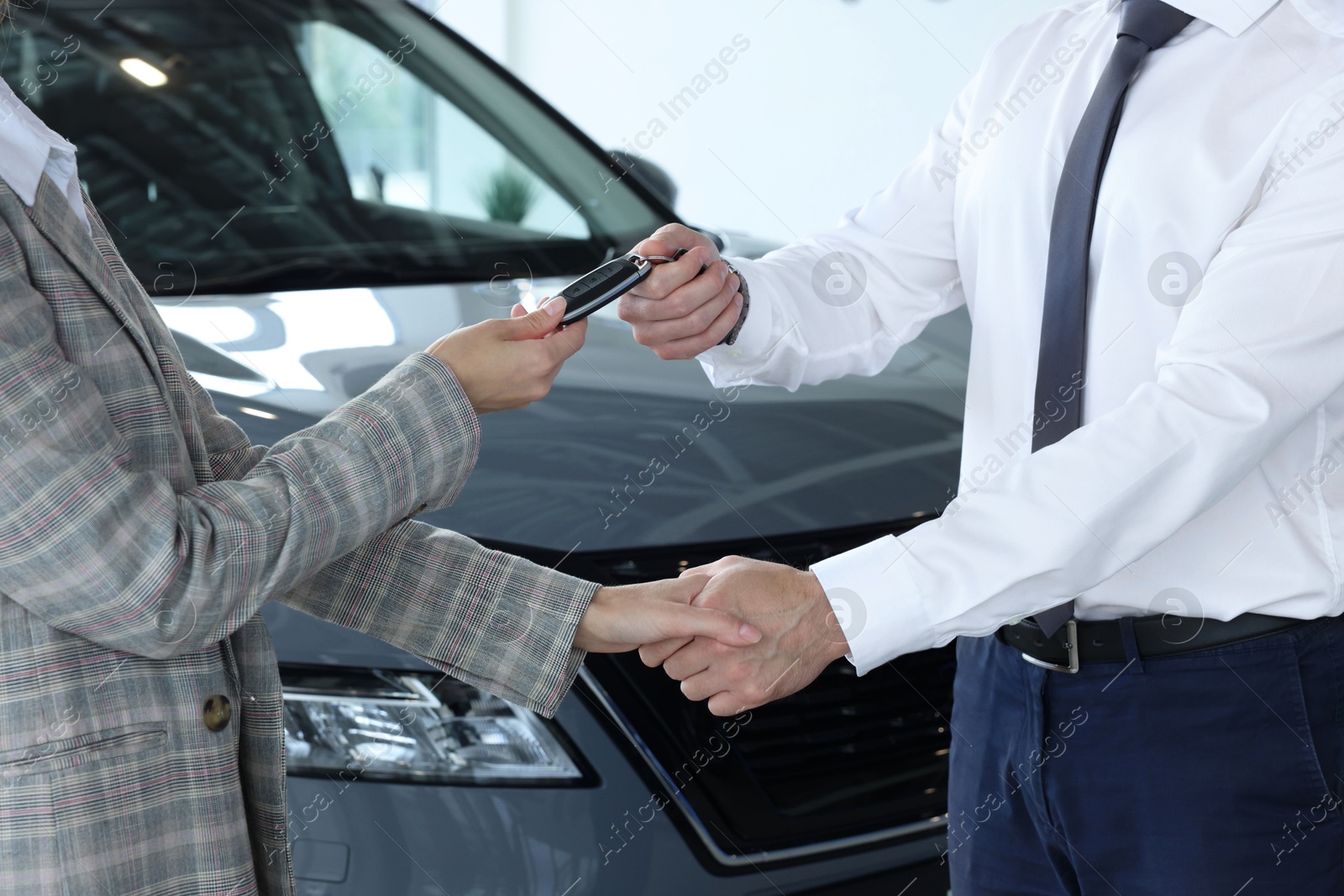 Photo of Salesman giving key to client near new car in salon, closeup