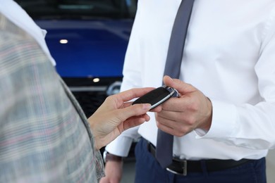 Photo of Saleswoman giving key to client near new car in salon, closeup