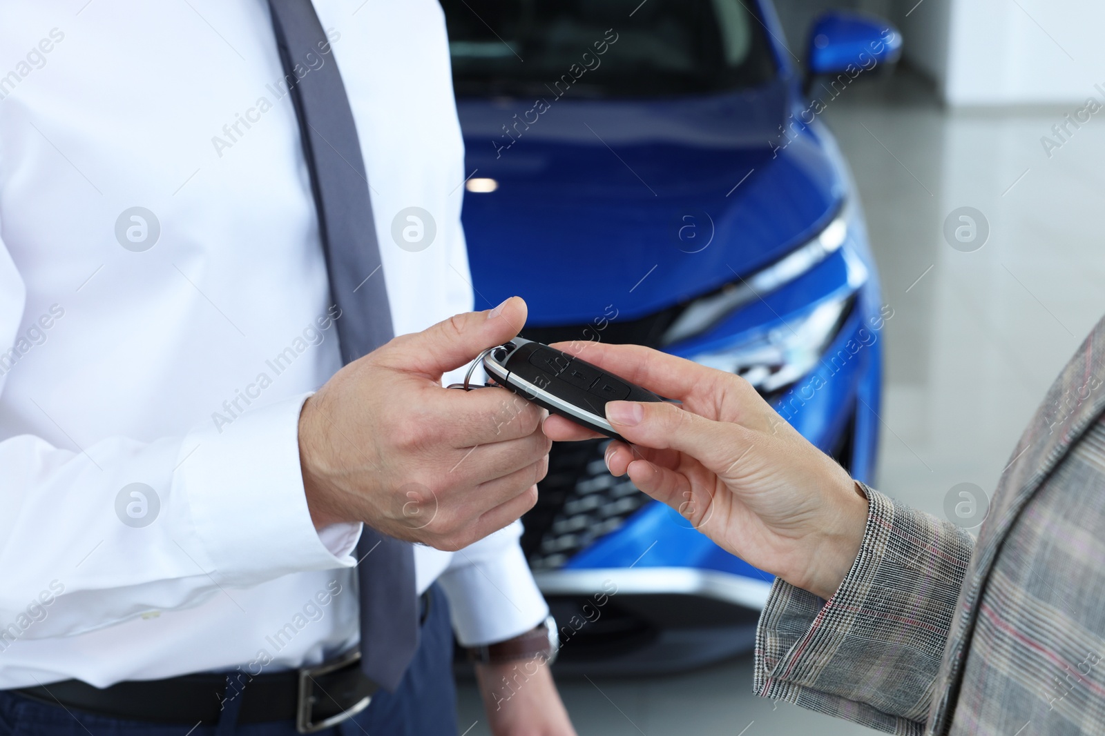 Photo of Saleswoman giving key to client near new car in salon, closeup