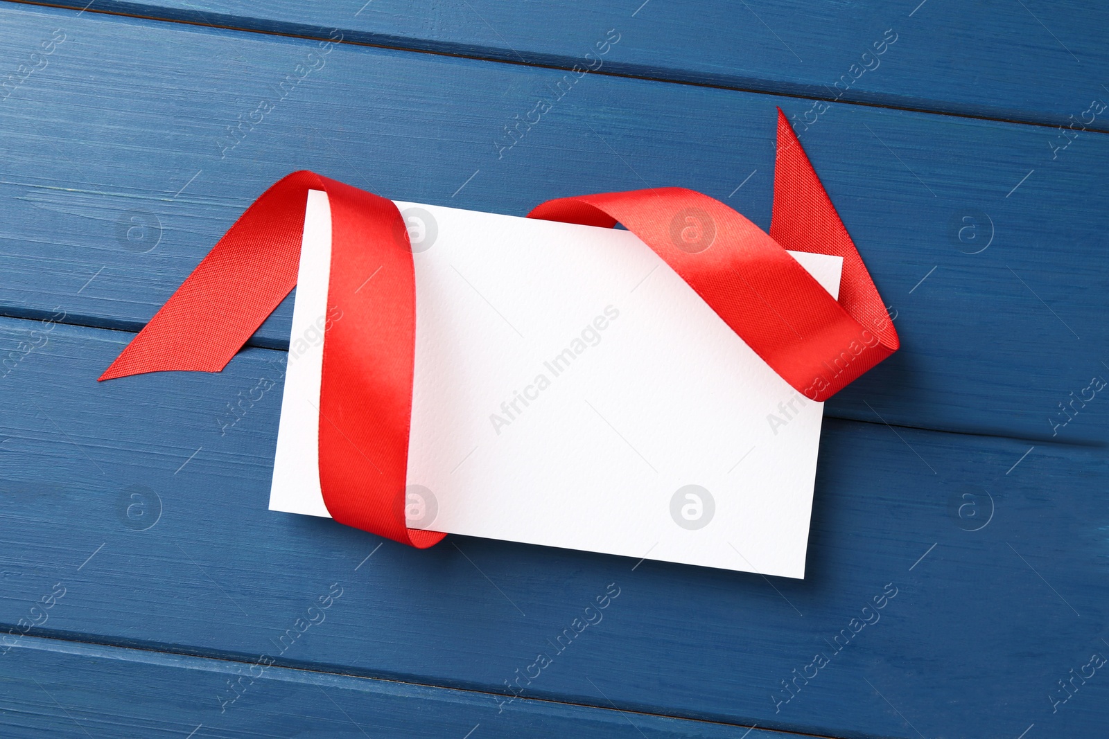 Photo of Blank card and red ribbon on blue wooden table, top view