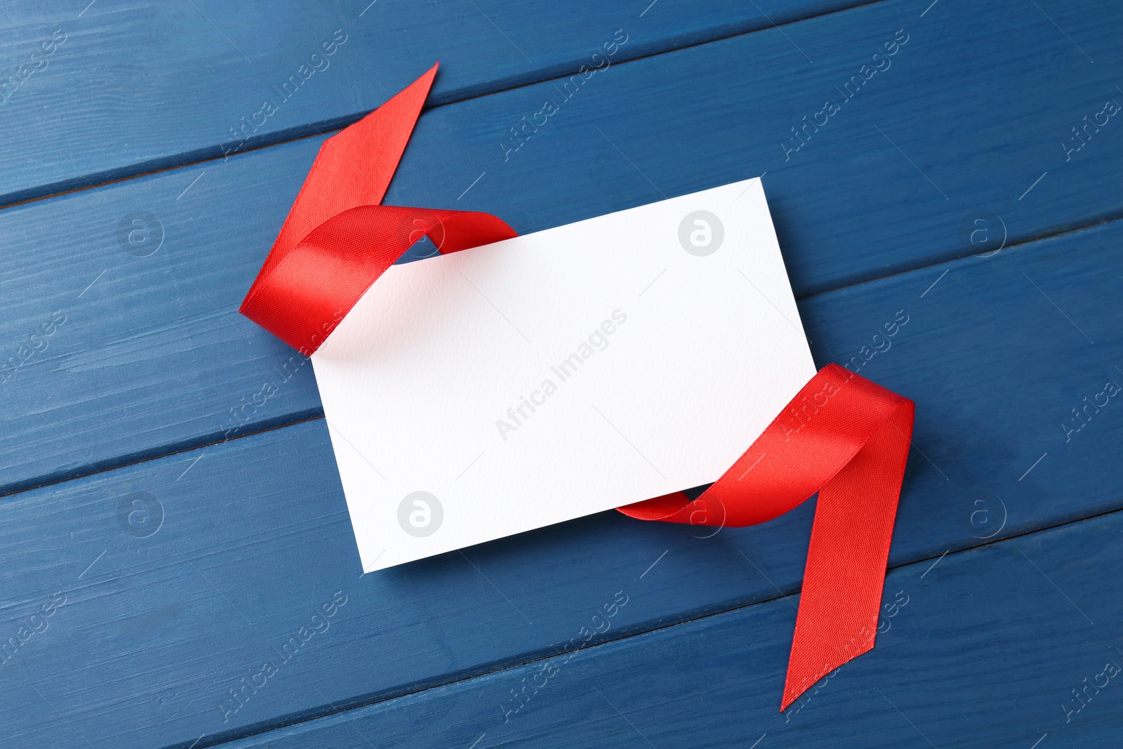 Photo of Blank card and red ribbon on blue wooden table, top view