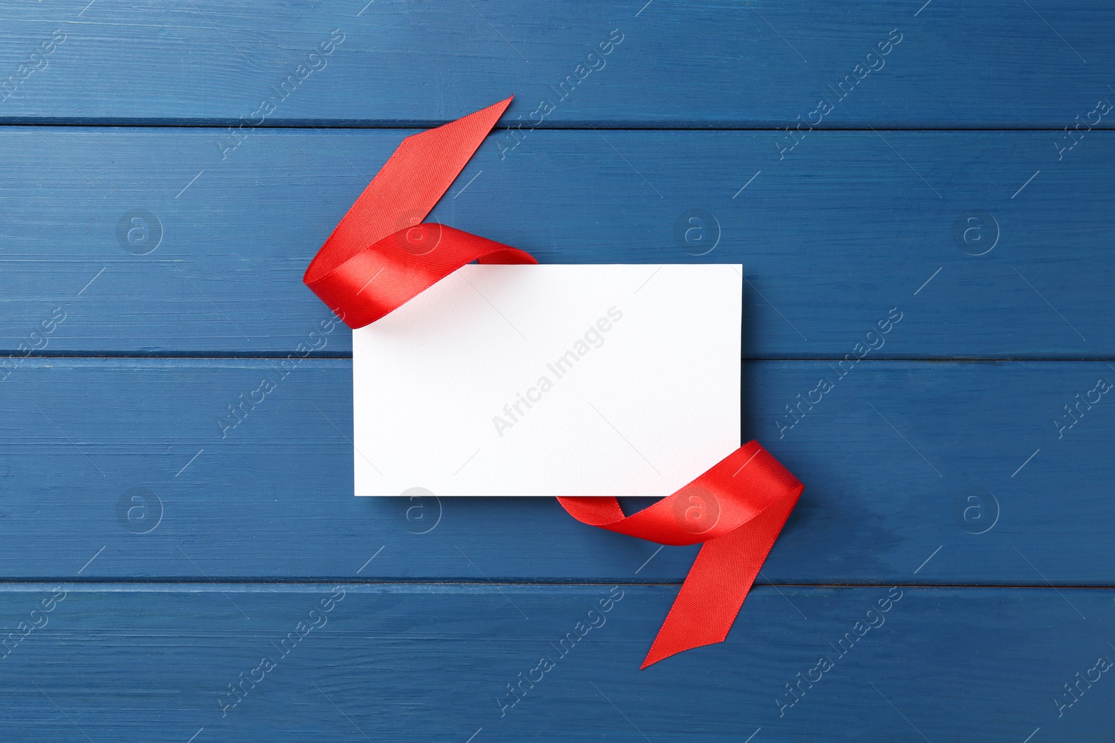 Photo of Blank card and red ribbon on blue wooden table, top view