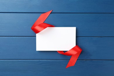 Photo of Blank card and red ribbon on blue wooden table, top view