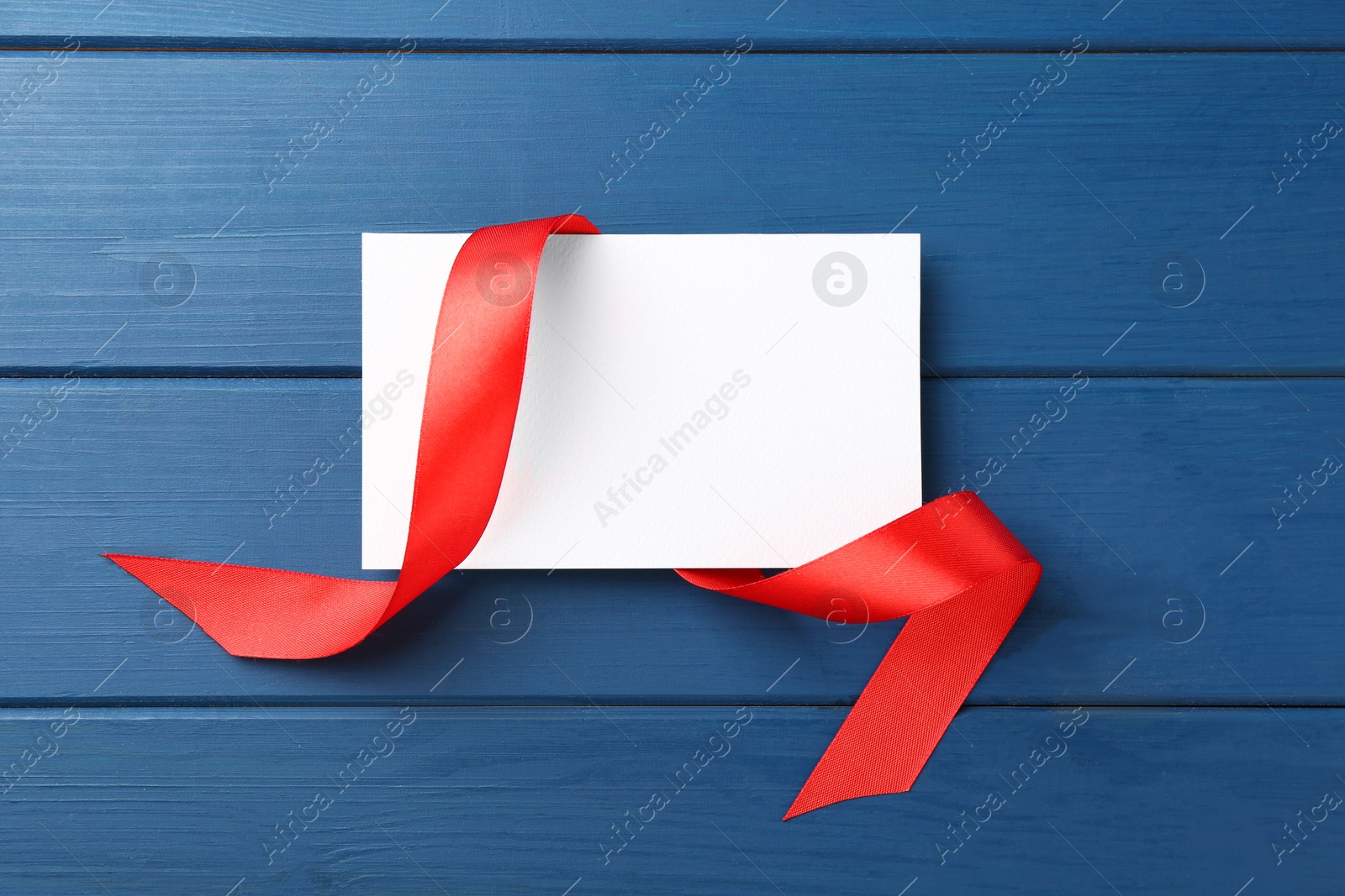 Photo of Blank card and red ribbon on blue wooden table, top view