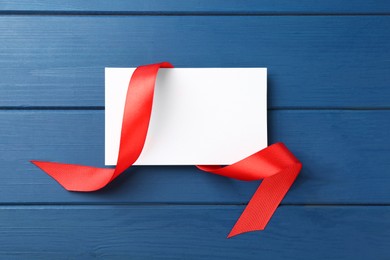 Photo of Blank card and red ribbon on blue wooden table, top view