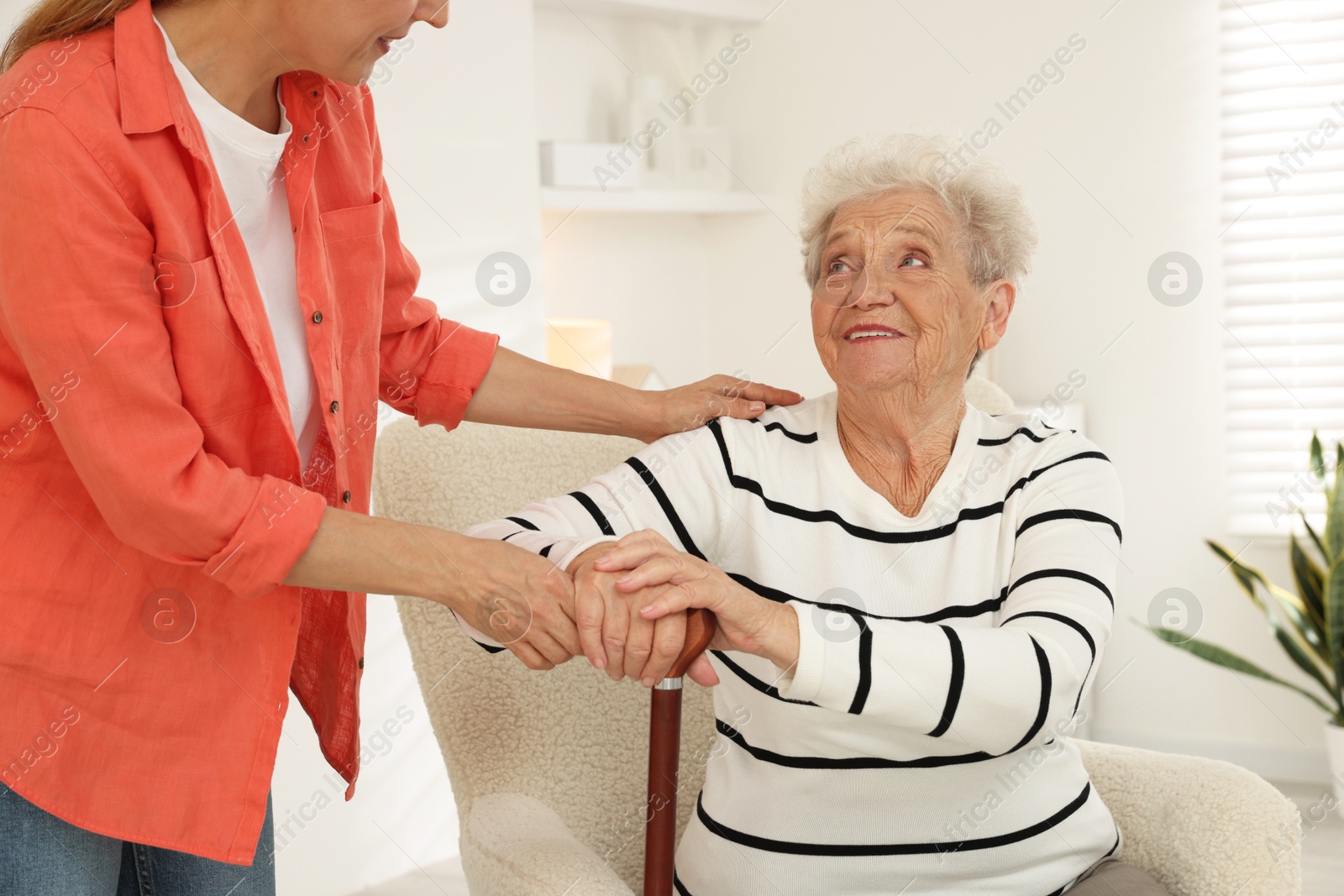 Photo of Caregiver supporting senior woman in living room at home