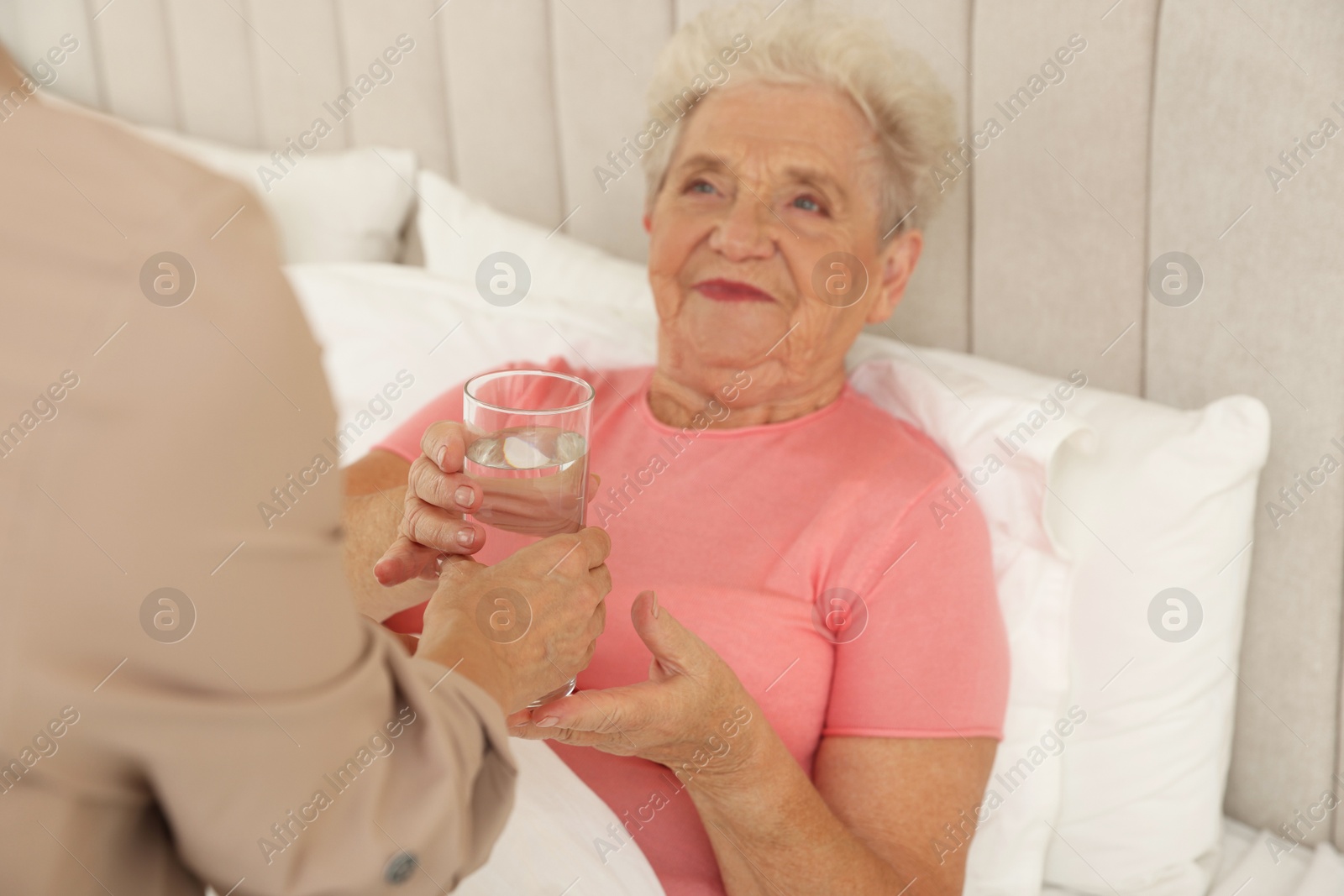 Photo of Caregiver giving glass of water to senior patient at home, selective focus