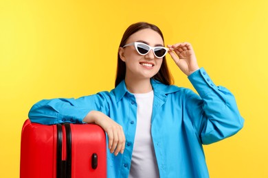 Photo of Woman with suitcase wearing sunglasses on orange background