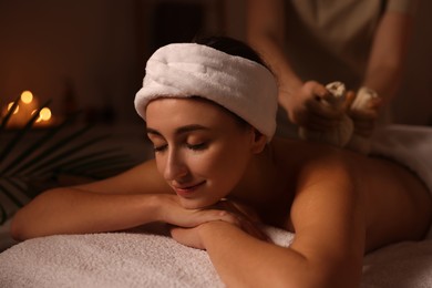 Photo of Young woman receiving back massage with herbal bags in spa salon