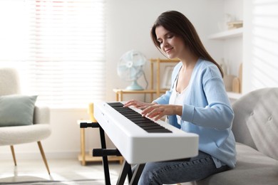 Photo of Beautiful woman playing synthesizer at home, space for text