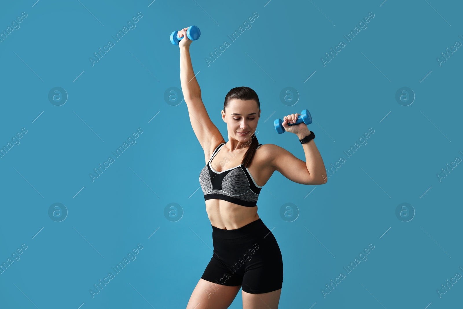 Photo of Woman in gym clothes exercising with dumbbells on light blue background