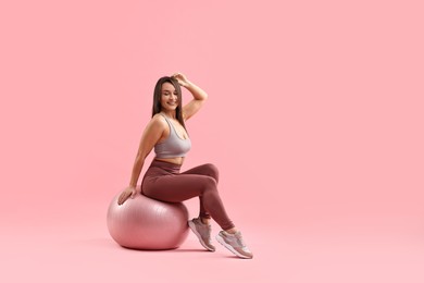 Photo of Woman in gym clothes with fitness ball on pink background