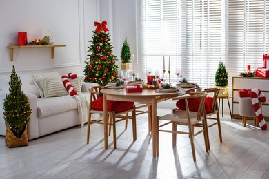 Photo of Christmas table setting with stylish dishware, glasses and burning candles in festive decorated room