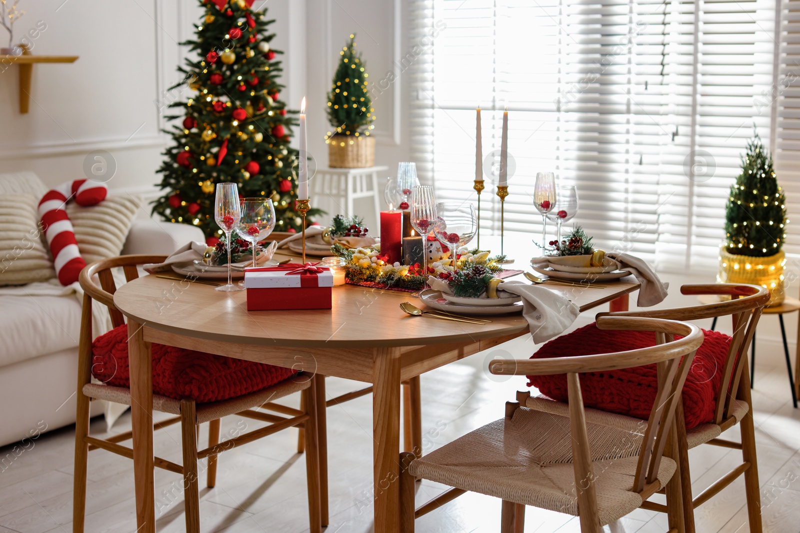 Photo of Christmas table setting with stylish dishware, glasses and burning candles in festive decorated room