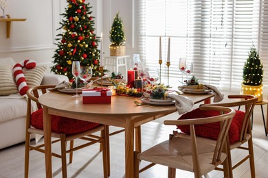 Photo of Christmas table setting with stylish dishware, glasses and burning candles in festive decorated room