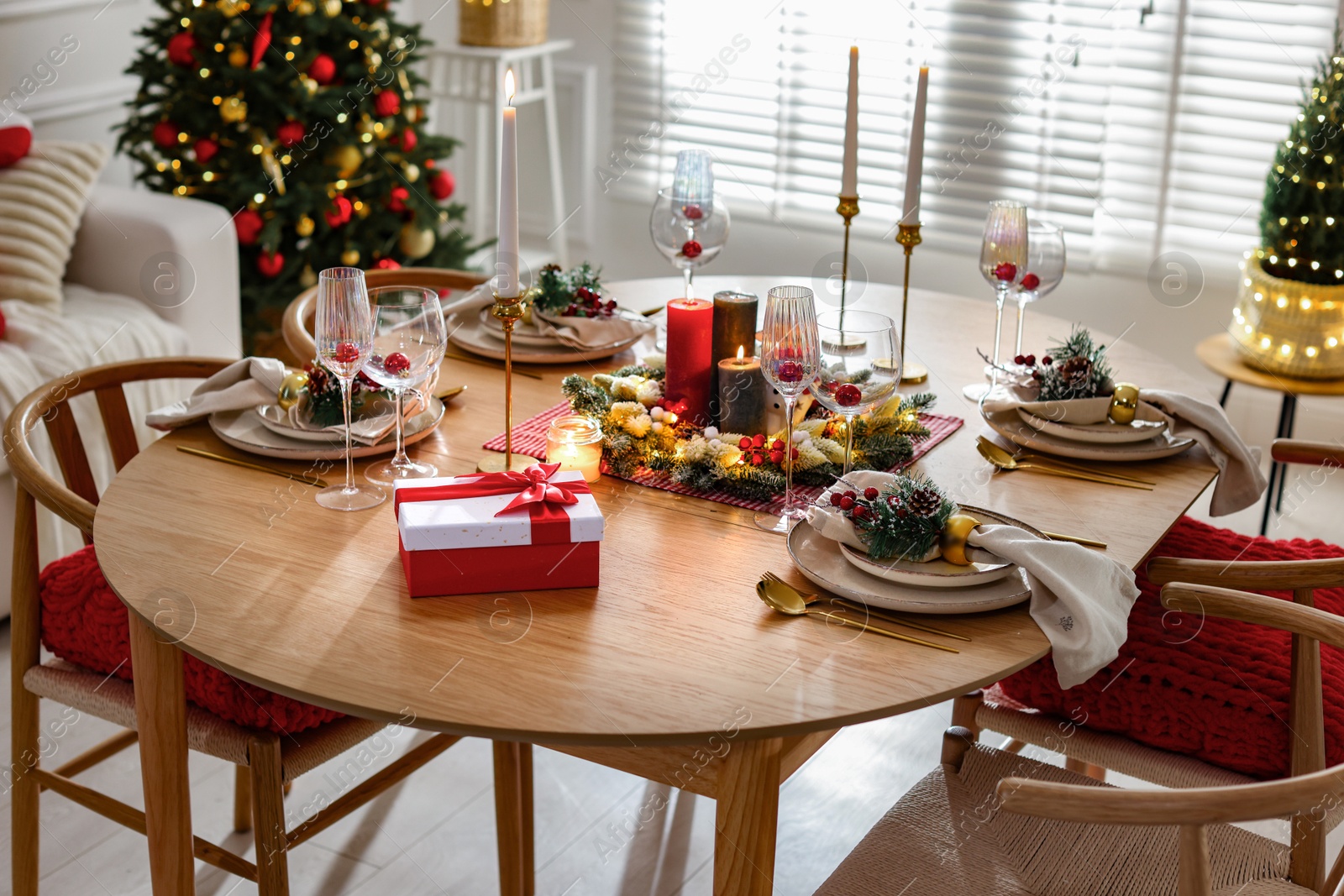 Photo of Christmas table setting with stylish dishware, glasses and burning candles in festive decorated room