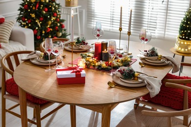 Photo of Christmas table setting with stylish dishware, glasses and burning candles in festive decorated room