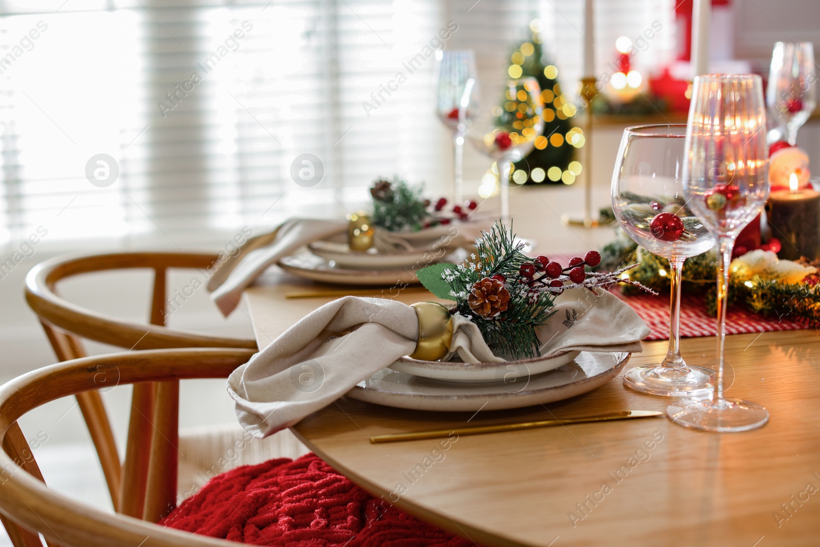 Photo of Christmas celebration. Festive table setting with dishware, glasses and decor in room, closeup