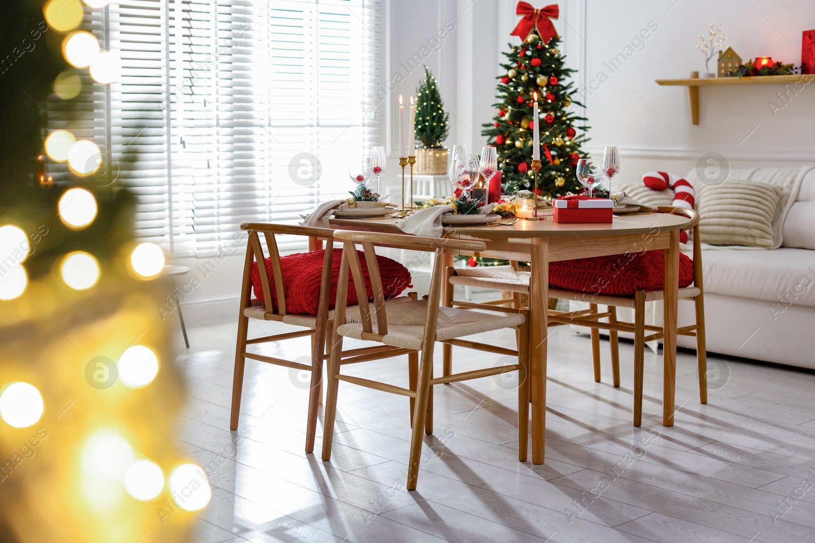 Photo of Christmas table setting with stylish dishware, glasses and burning candles in festive decorated room