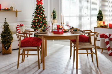 Photo of Christmas table setting with stylish dishware, glasses and burning candles in festive decorated room