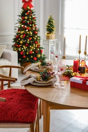 Photo of Christmas table setting with stylish dishware, glasses and burning candles in festive decorated room