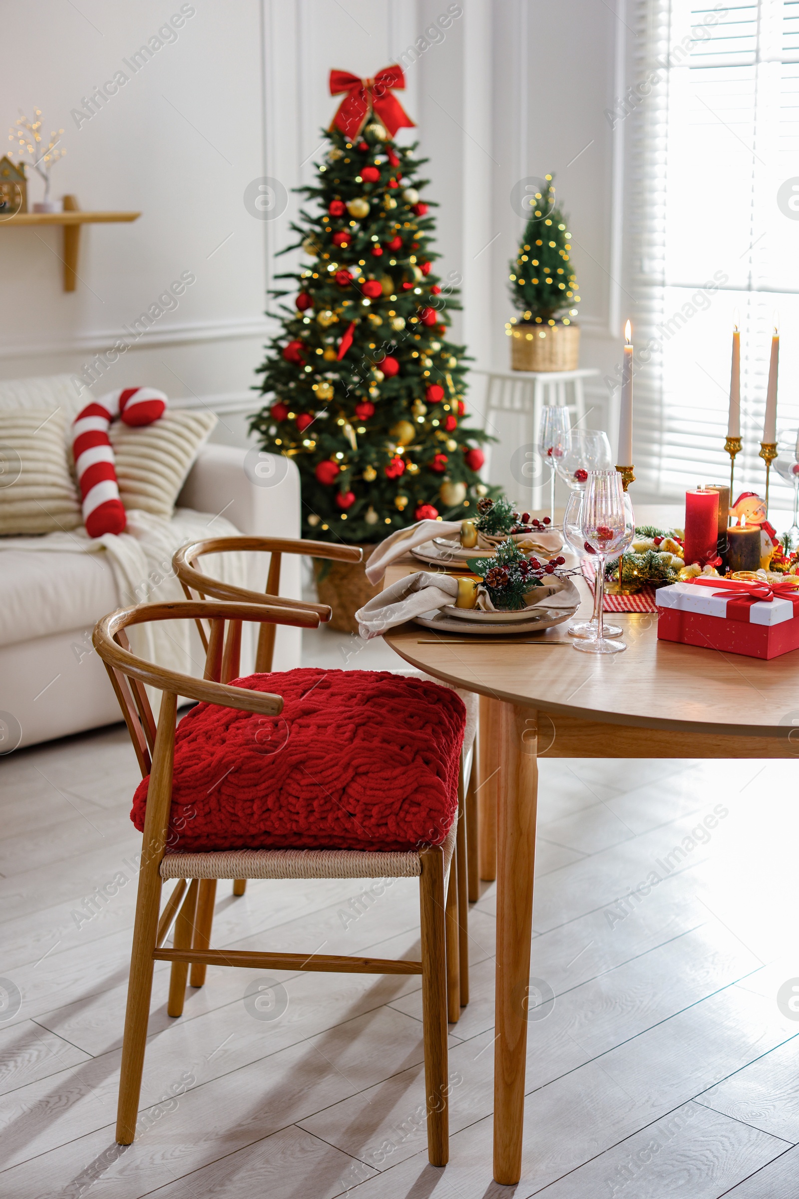 Photo of Christmas table setting with stylish dishware, glasses and burning candles in festive decorated room