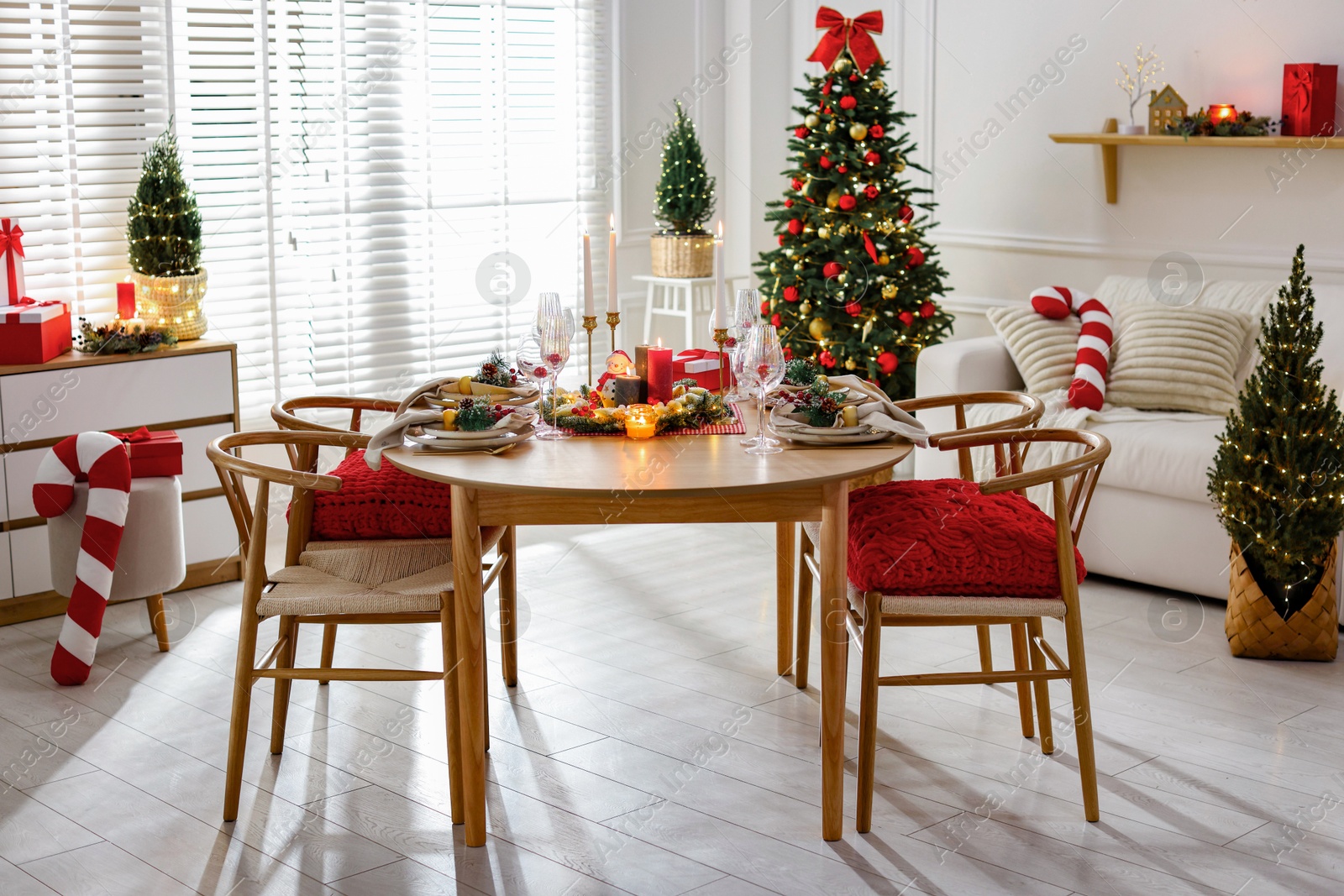 Photo of Christmas table setting with stylish dishware, glasses and burning candles in festive decorated room