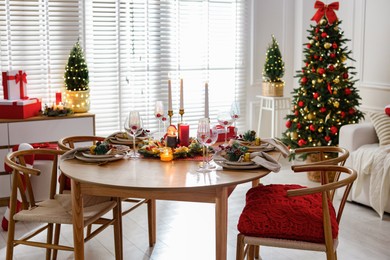 Photo of Christmas table setting with stylish dishware, glasses and burning candles in festive decorated room