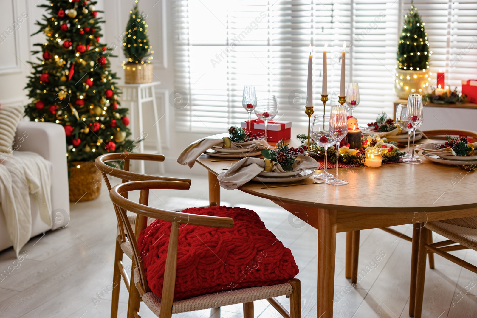 Photo of Christmas table setting with stylish dishware, glasses and burning candles in festive decorated room