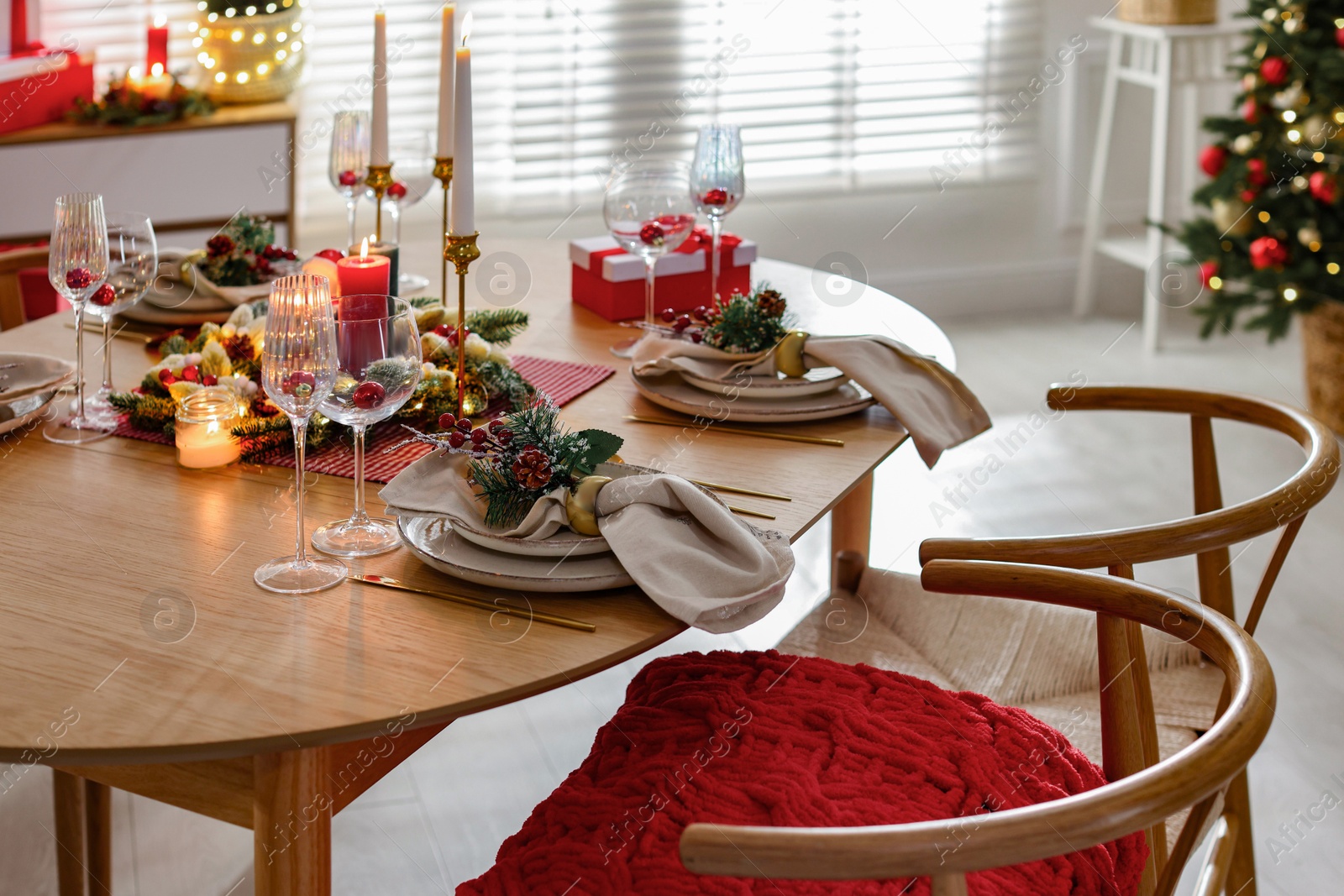 Photo of Christmas celebration. Festive table setting with dishware, glasses and decor in room