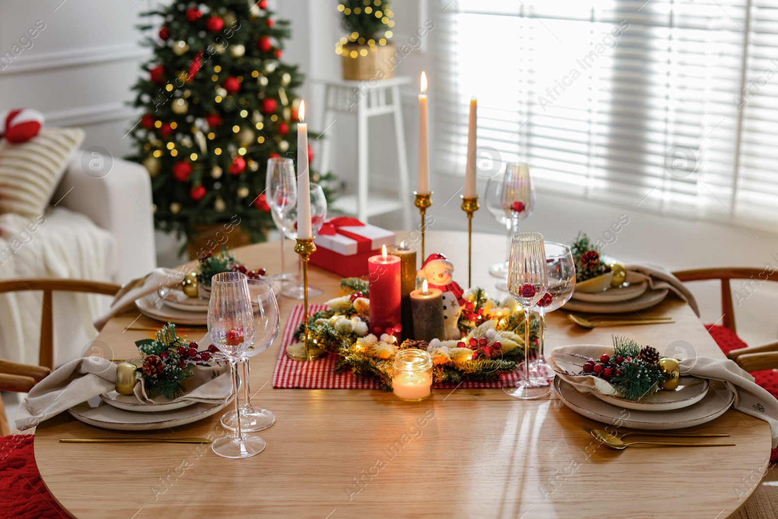 Photo of Christmas table setting with stylish dishware, glasses and burning candles in festive decorated room