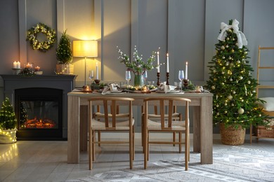 Photo of Christmas table setting with stylish dishware, glasses and burning candles in festive decorated room