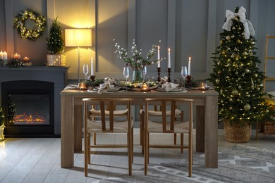 Photo of Christmas table setting with stylish dishware, glasses and burning candles in festive decorated room