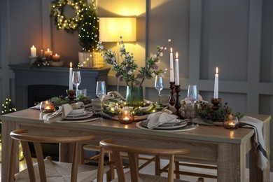 Photo of Christmas table setting with stylish dishware, glasses and burning candles in festive decorated room