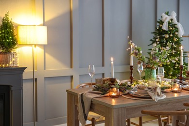 Photo of Christmas table setting with stylish dishware, glasses and burning candles in festive decorated room