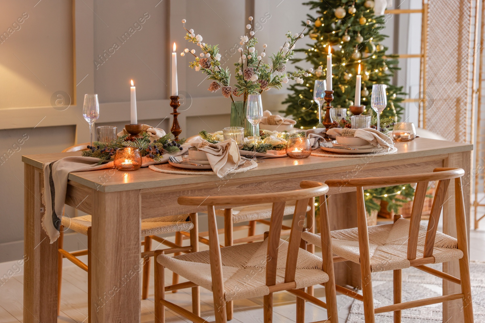 Photo of Christmas table setting with stylish dishware, glasses and burning candles in festive decorated room