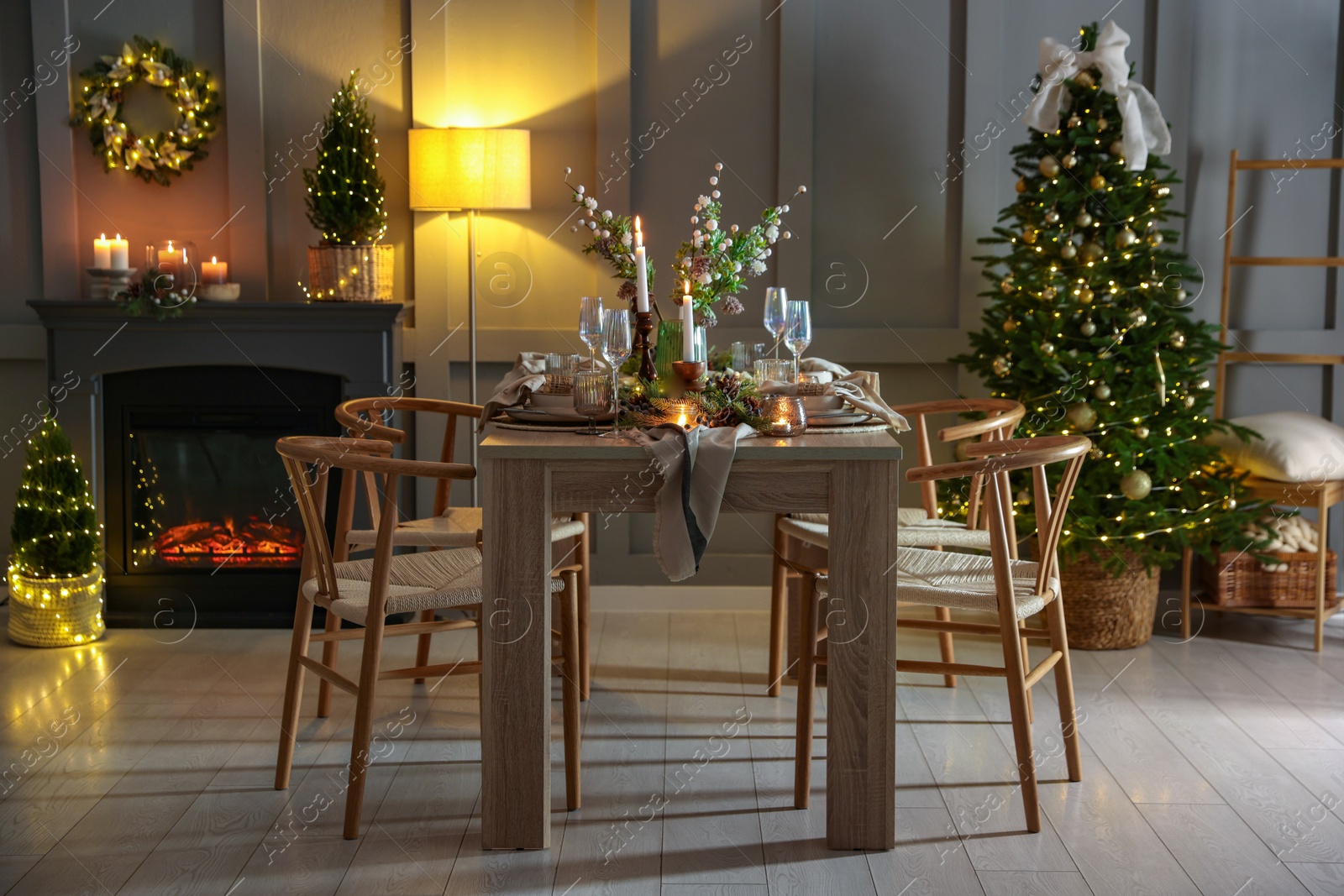 Photo of Christmas table setting with stylish dishware, glasses and burning candles in festive decorated room