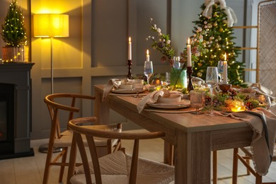 Photo of Christmas table setting with stylish dishware, glasses and burning candles in festive decorated room