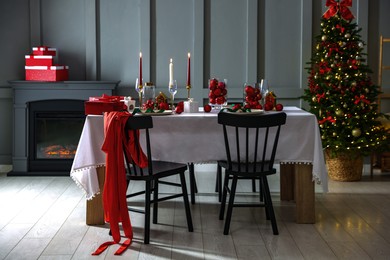 Photo of Christmas table setting with stylish dishware, glasses and burning candles in festive decorated room