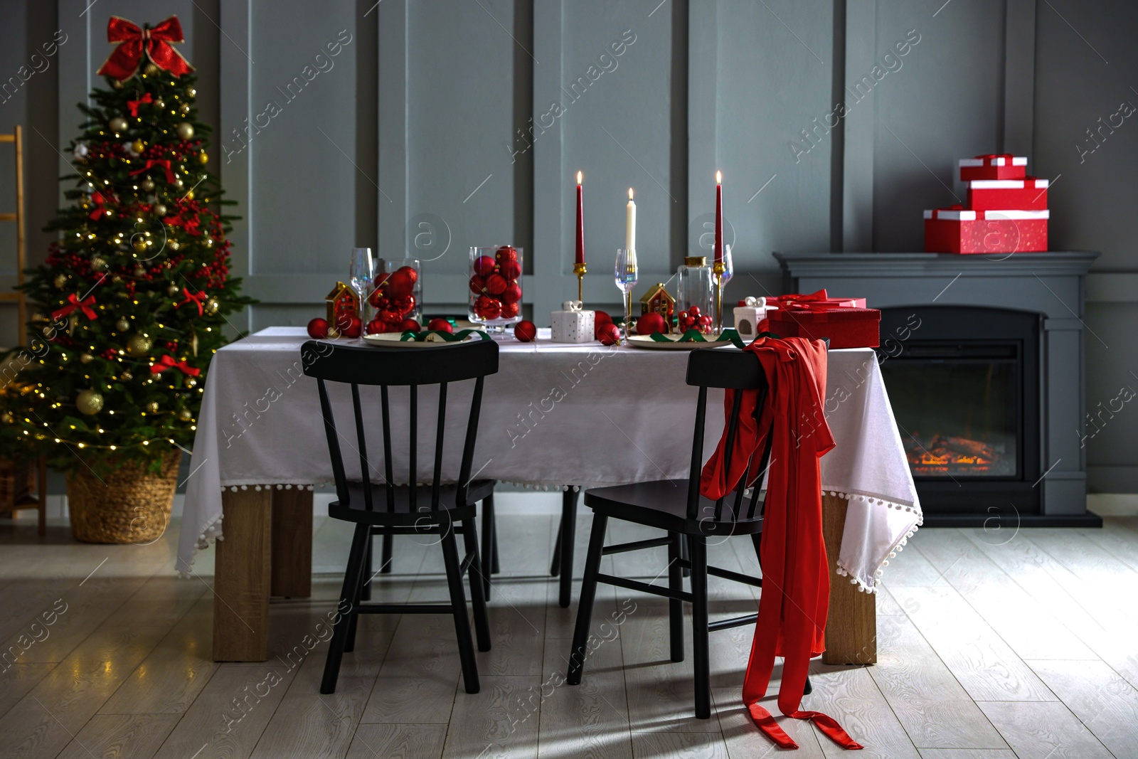 Photo of Christmas table setting with stylish dishware, glasses and burning candles in festive decorated room