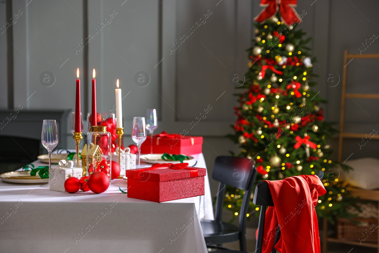 Photo of Christmas table setting with stylish dishware, glasses and burning candles in festive decorated room