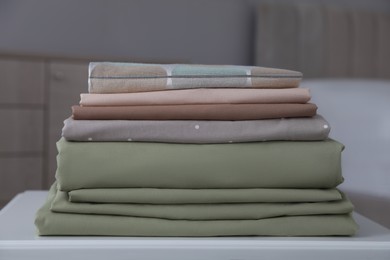 Photo of New clean folded bed linens on table indoors