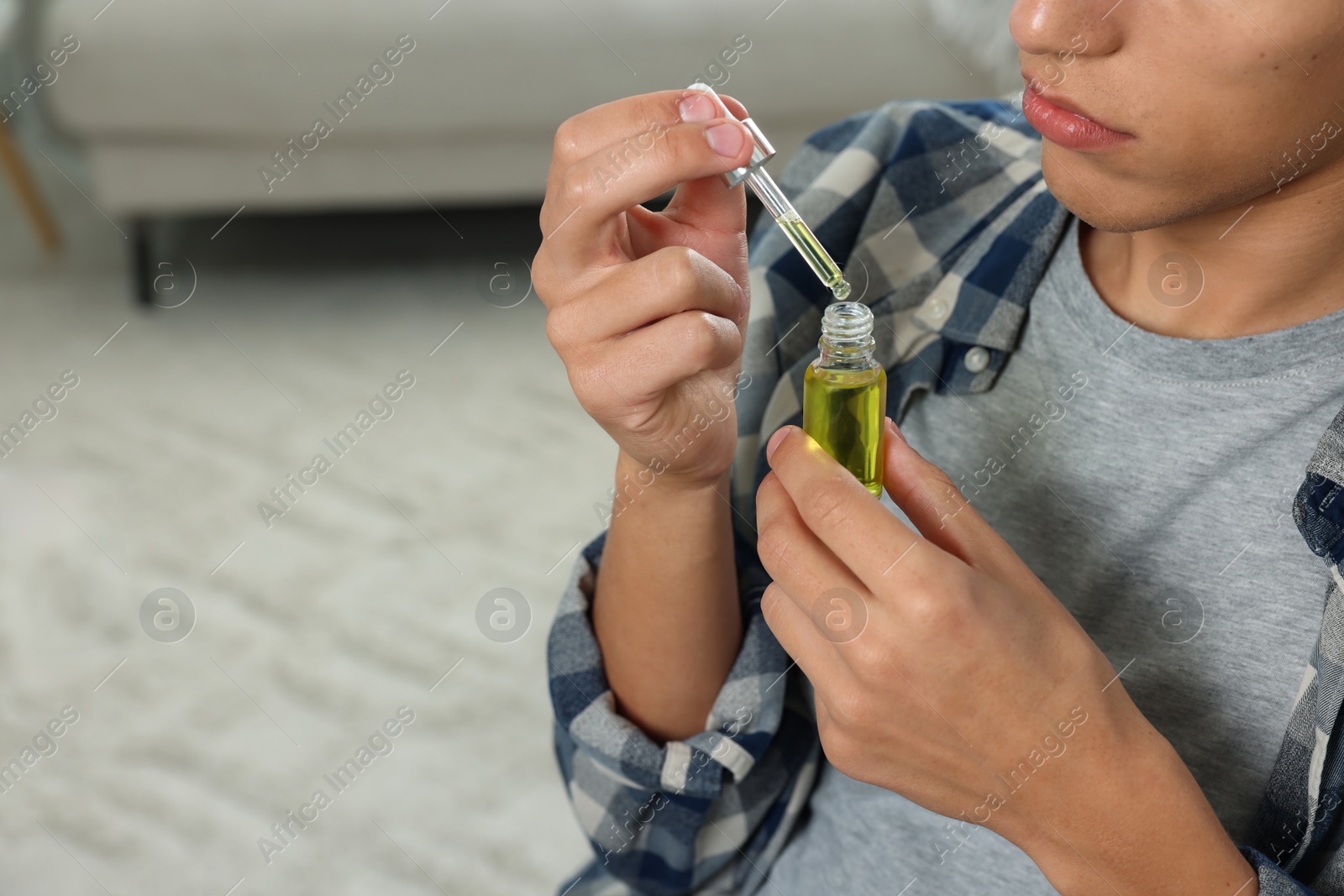 Photo of Young man taking CBD tincture indoors, closeup. Space for text