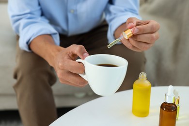 Photo of Young man dripping CBD tincture into drink at white table, closeup