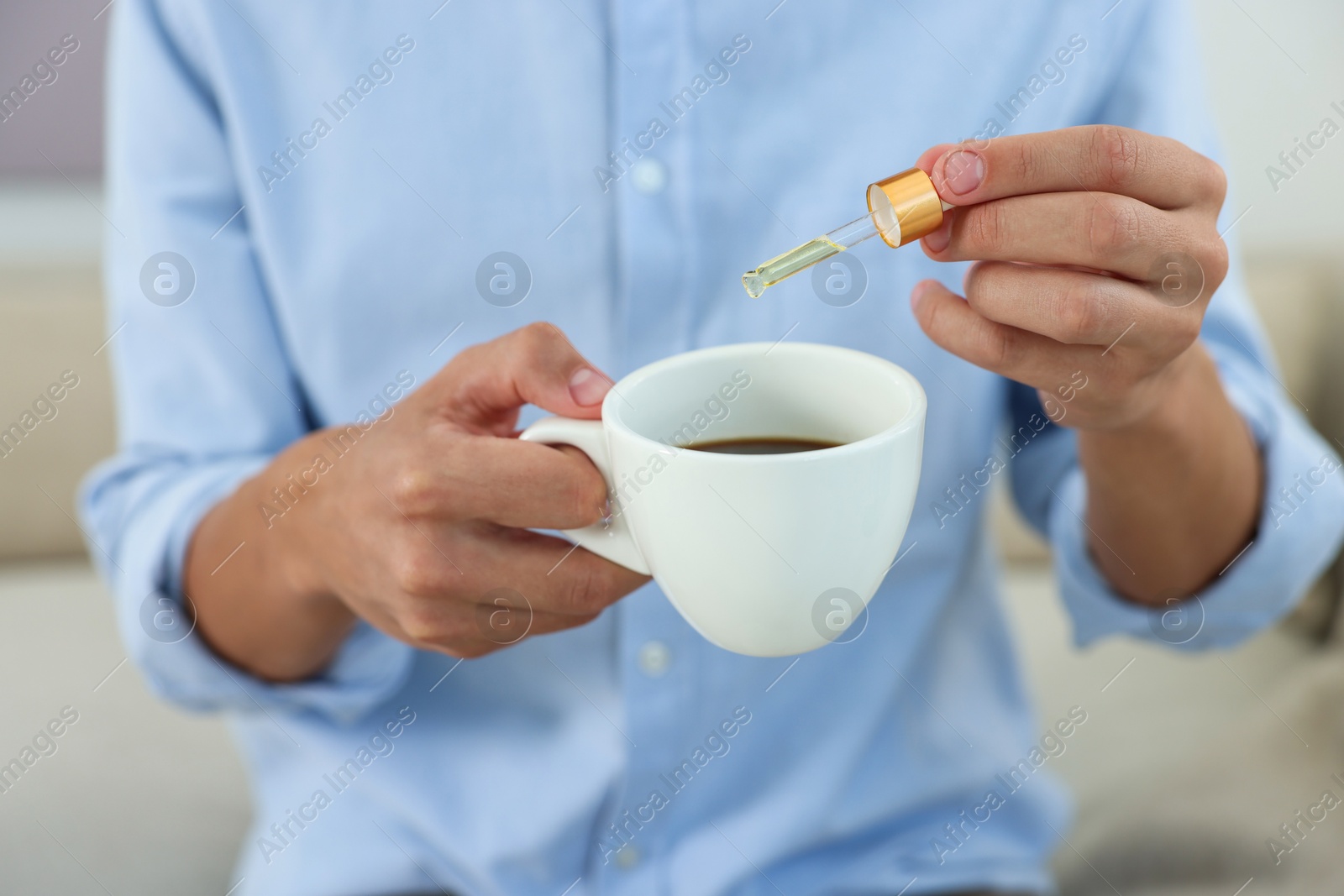 Photo of Young man dripping CBD tincture into drink indoors, closeup