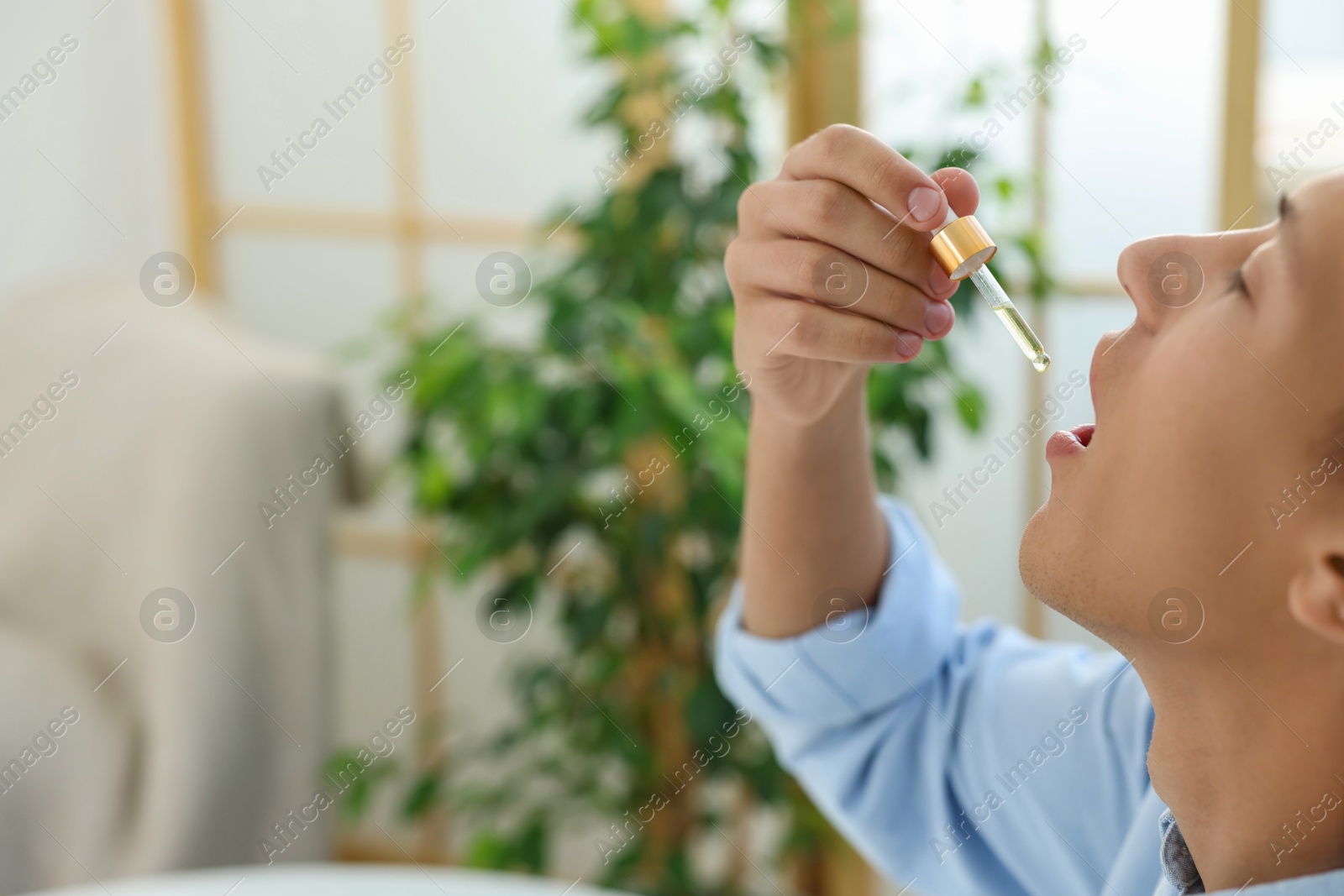 Photo of Young man taking CBD tincture indoors, space for text