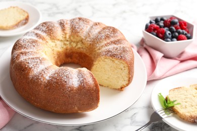 Photo of Freshly baked sponge cake, mint and berries on white marble table, closeup