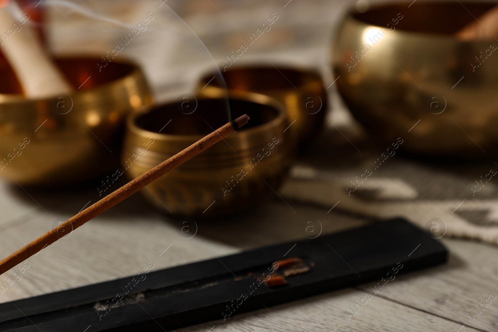 Photo of Incense stick smoldering in holder and tibetan singing bowls on floor, closeup