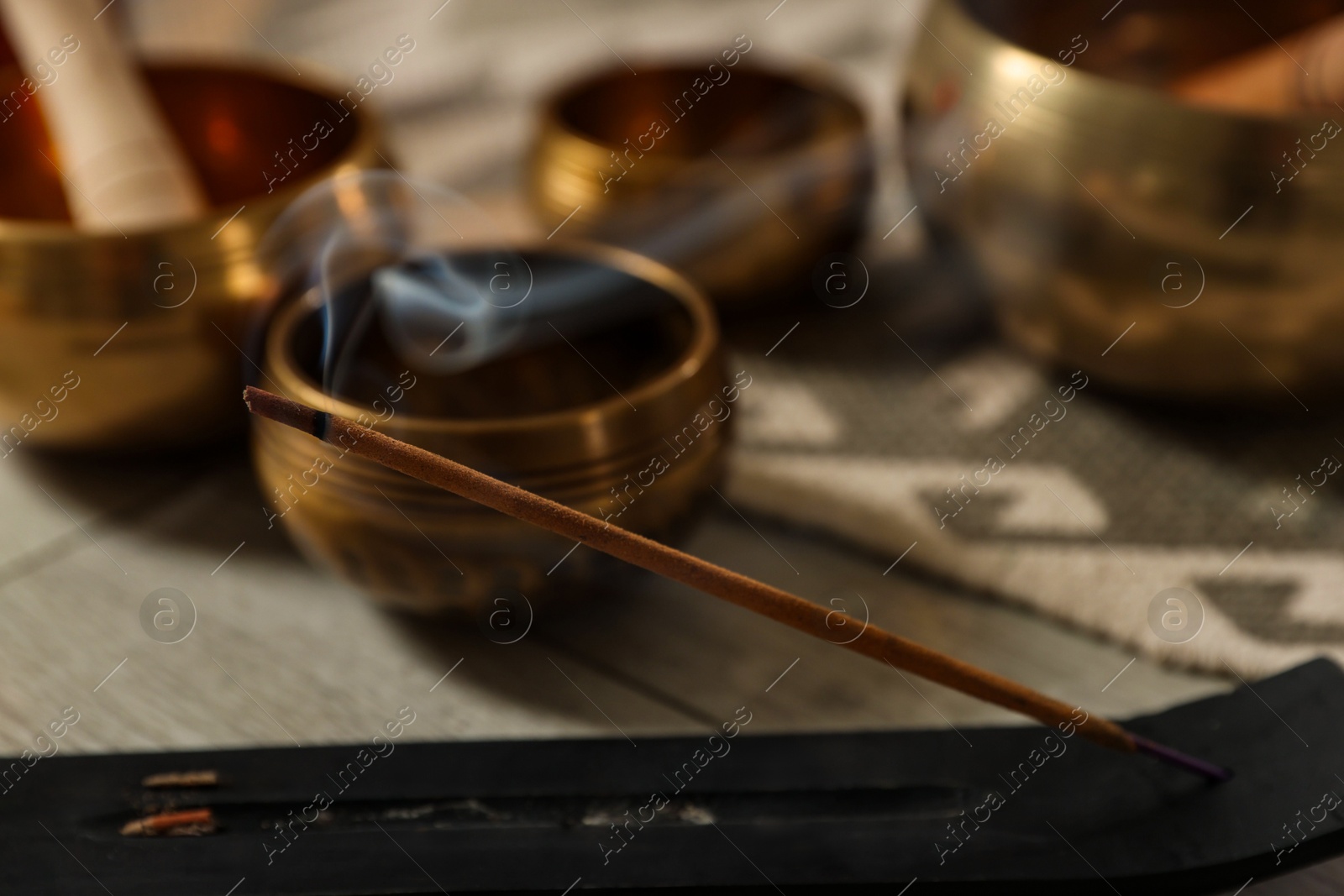 Photo of Incense stick smoldering in holder and tibetan singing bowls on floor, closeup